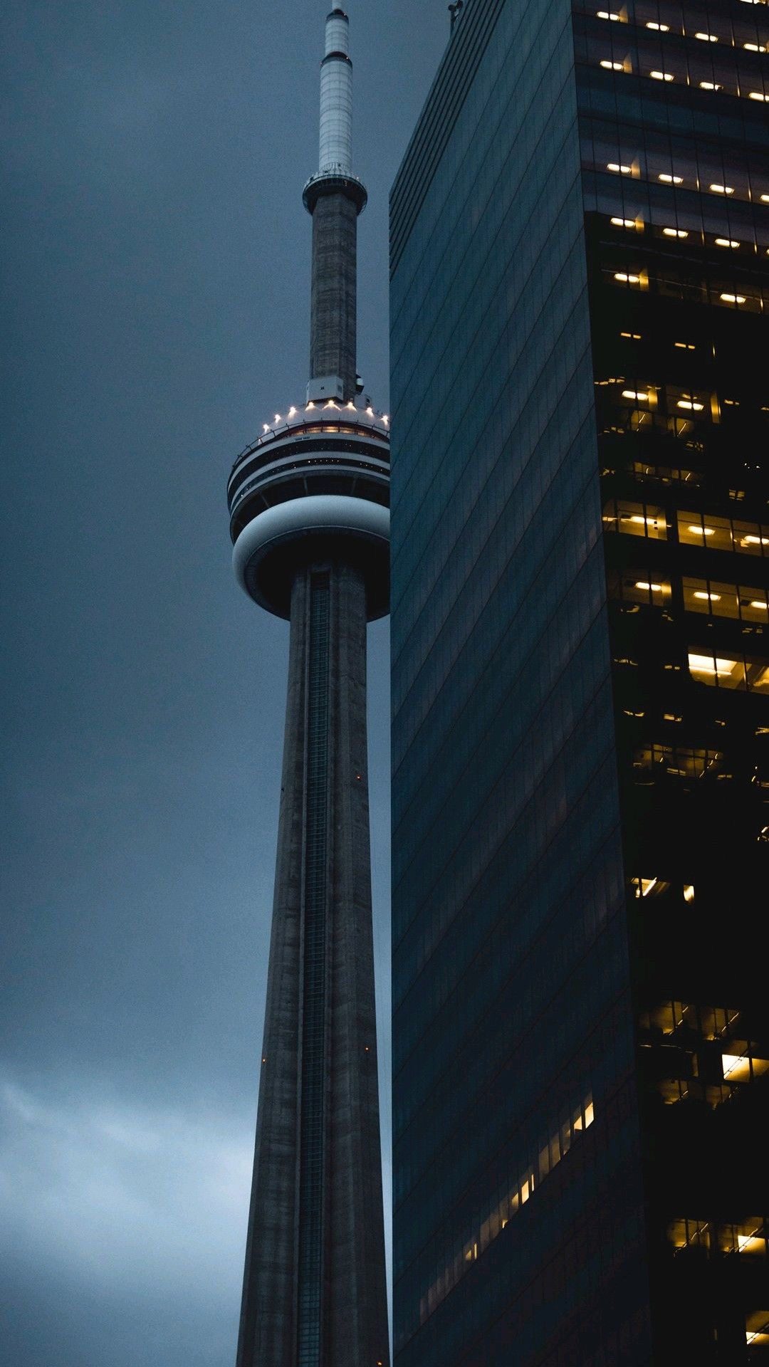 The CN Tower observation deck rising beside a glass office tower in the blue-grey light of dusk, downtown Toronto